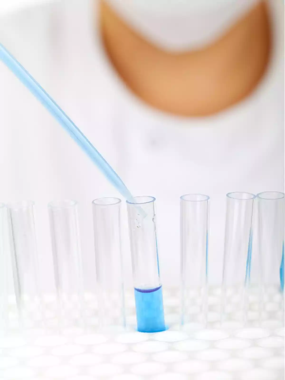 Persona usando una pipeta para transferir líquido azul a un tubo de ensayo en un laboratorio.