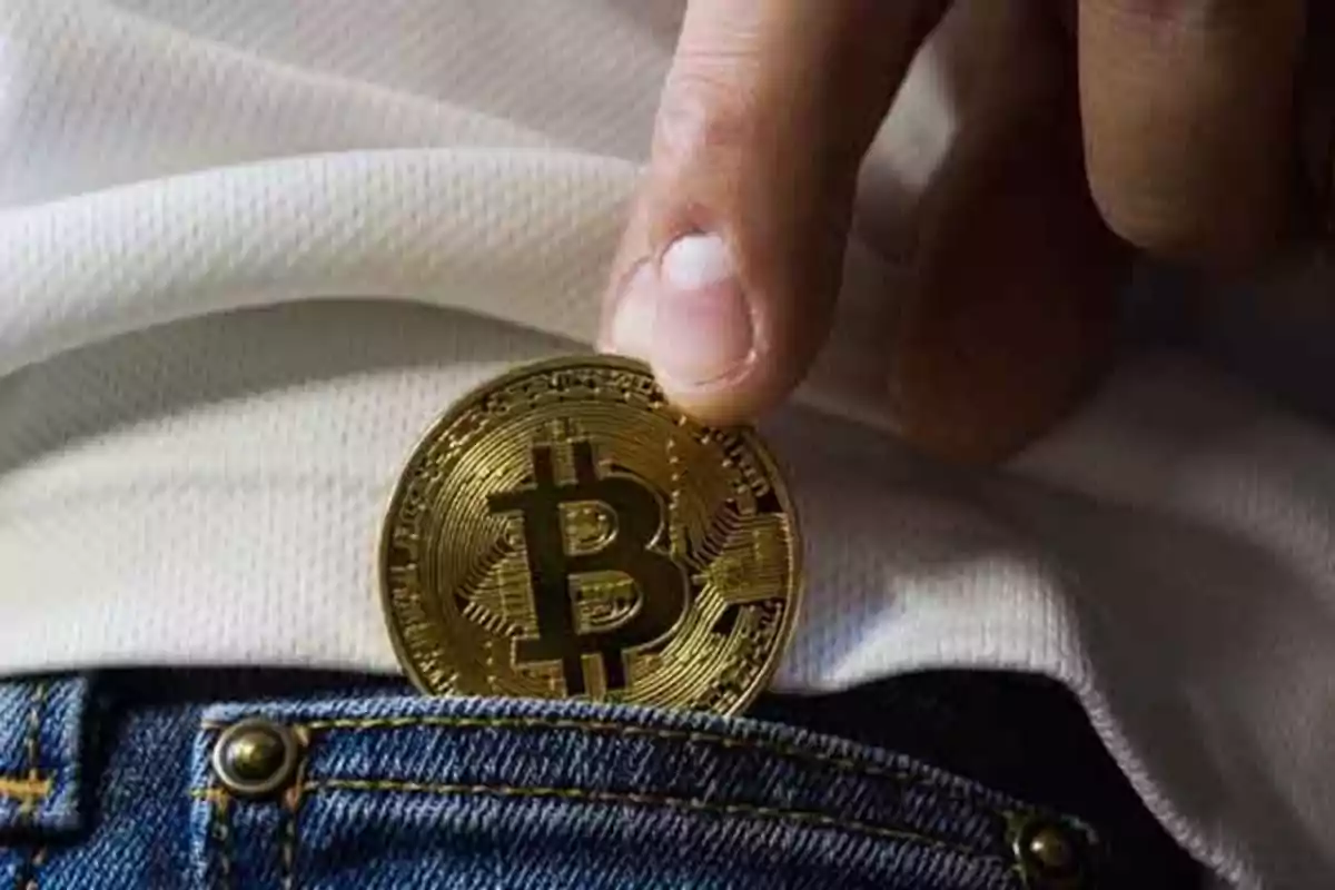 Una mano sosteniendo una moneda de Bitcoin sobre un bolsillo de mezclilla.