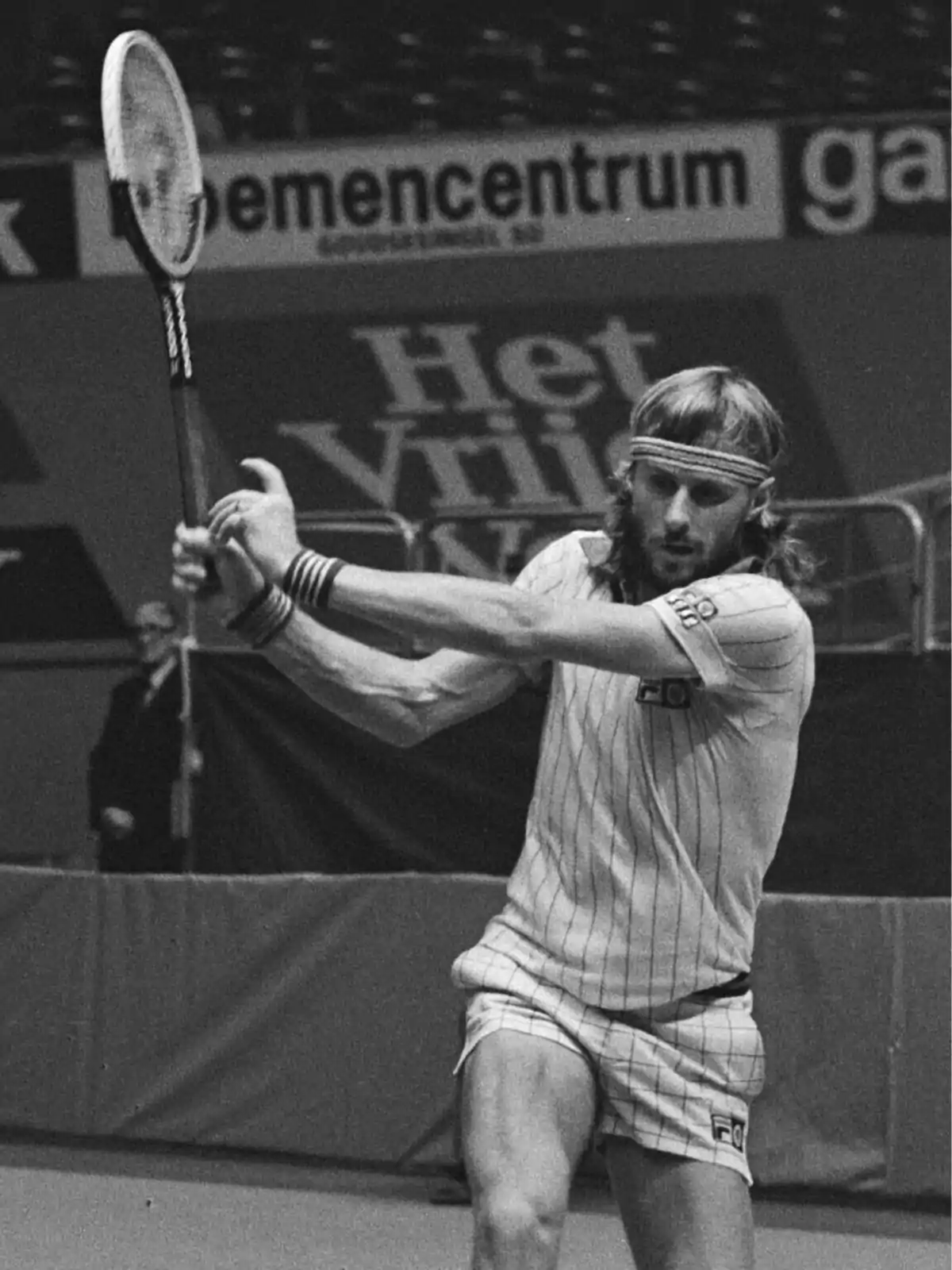 Jugador de tenis en acción durante un partido en una cancha cubierta, vistiendo ropa deportiva clásica y sosteniendo una raqueta.
