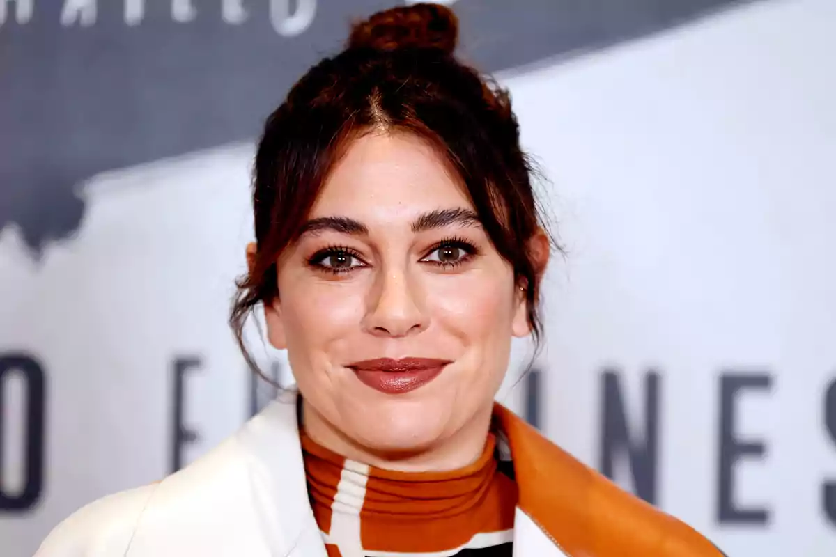 Una persona con cabello oscuro y recogido sonríe frente a un fondo borroso.