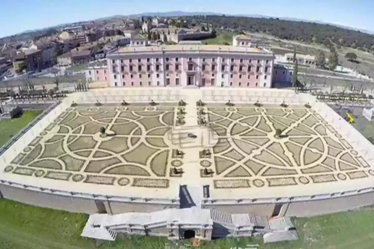 Vista aérea de un jardín formal con un edificio grande al fondo y una ciudad en el horizonte.