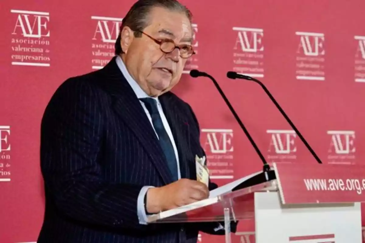 Un hombre hablando en un podio con un fondo rojo que tiene el logo de la Asociación Valenciana de Empresarios.