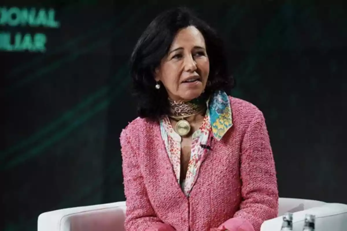 Mujer con chaqueta rosa y bufanda colorida sentada en un sillón blanco.