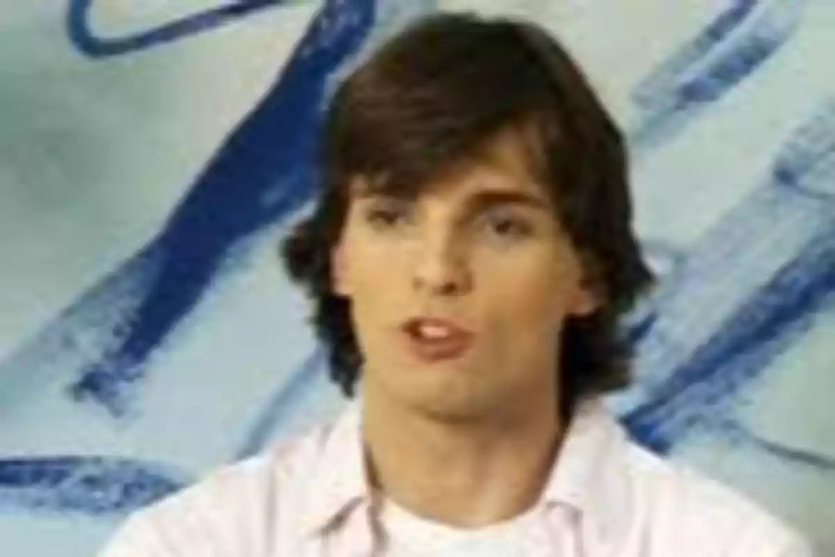 Un hombre joven con cabello castaño y una camisa clara está frente a un fondo con trazos azules. Un hombre joven con cabello castaño y una camisa clara está frente a un fondo con trazos azules.
