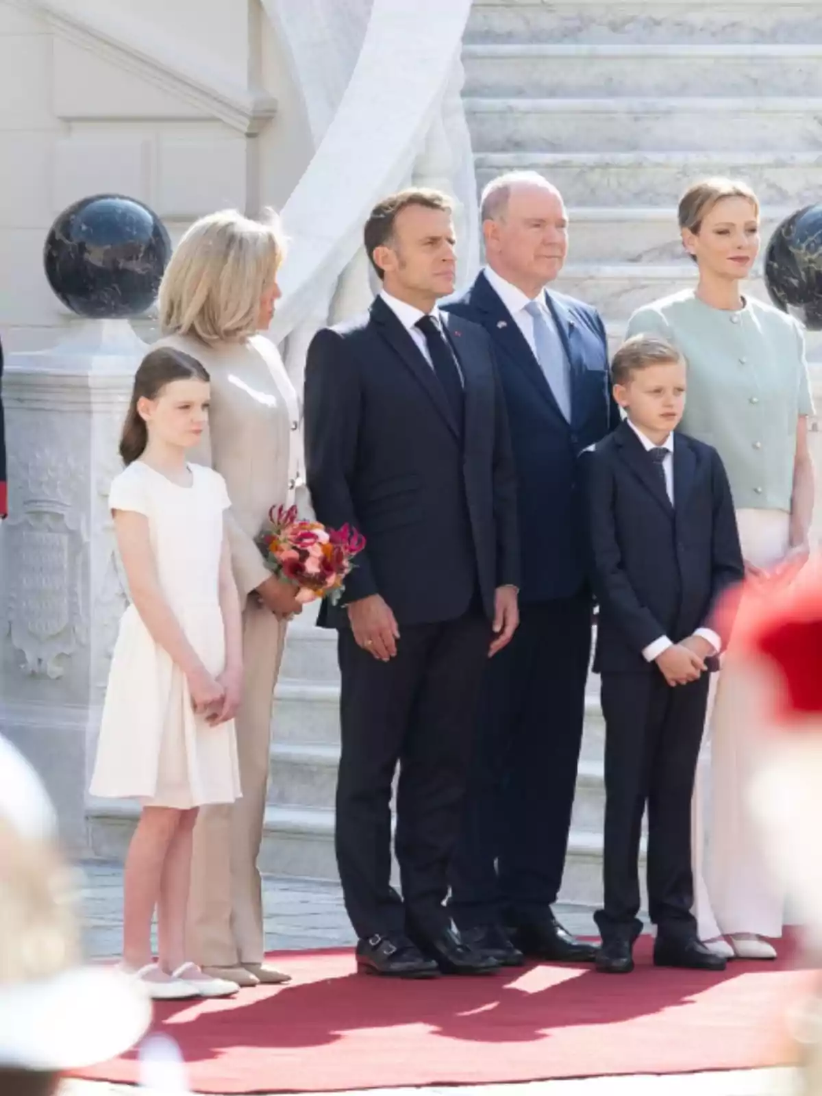 Grupo de seis personas elegantemente vestidas posando sobre una alfombra roja frente a una escalera de mármol Grupo de seis personas elegantemente vestidas posando sobre una alfombra roja frente a una escalera de mármol