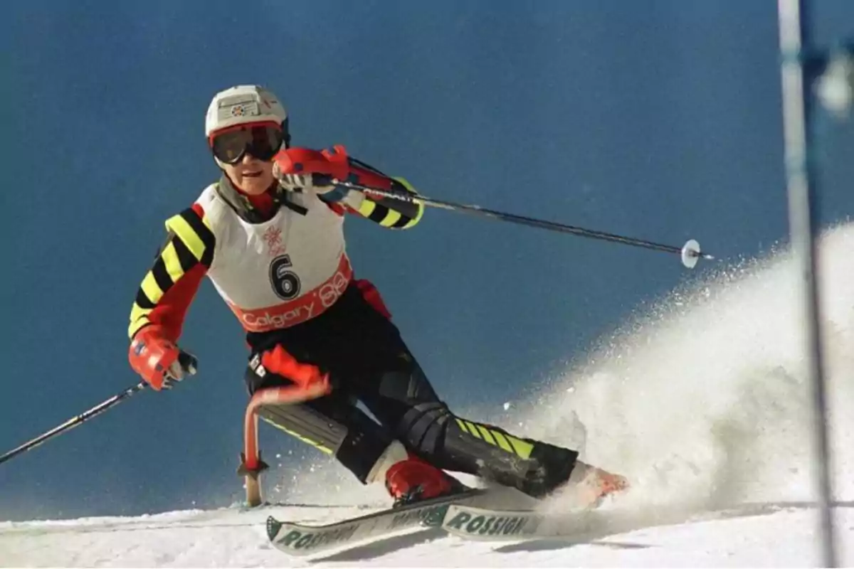 Esquiador en plena acción durante una competencia de esquí alpino, vistiendo un uniforme rojo y negro con el número 6 y un casco blanco.