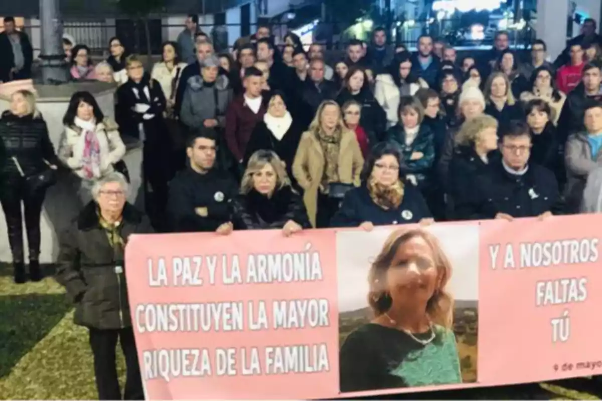 Un grupo de personas se reúne sosteniendo una pancarta rosa con un mensaje sobre la paz y la armonía familiar, junto a una foto de una mujer.