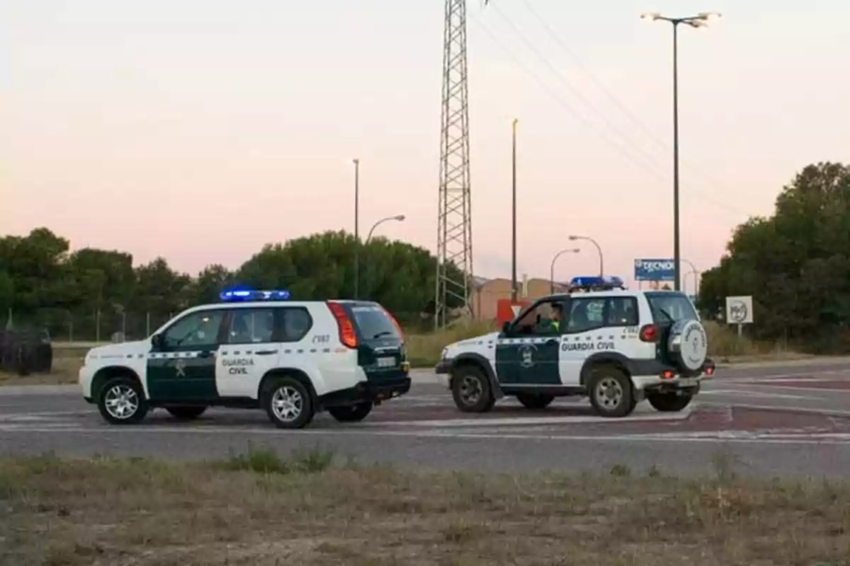 Dos vehículos de la Guardia Civil en una intersección de carretera con luces azules encendidas.