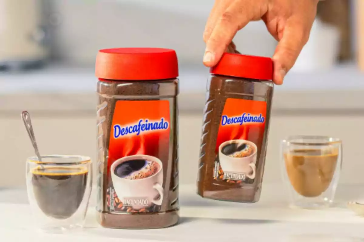 Dos frascos de café descafeinado con tapas rojas junto a dos tazas de café en una mesa. Dos frascos de café descafeinado con tapas rojas junto a dos tazas de café en una mesa.