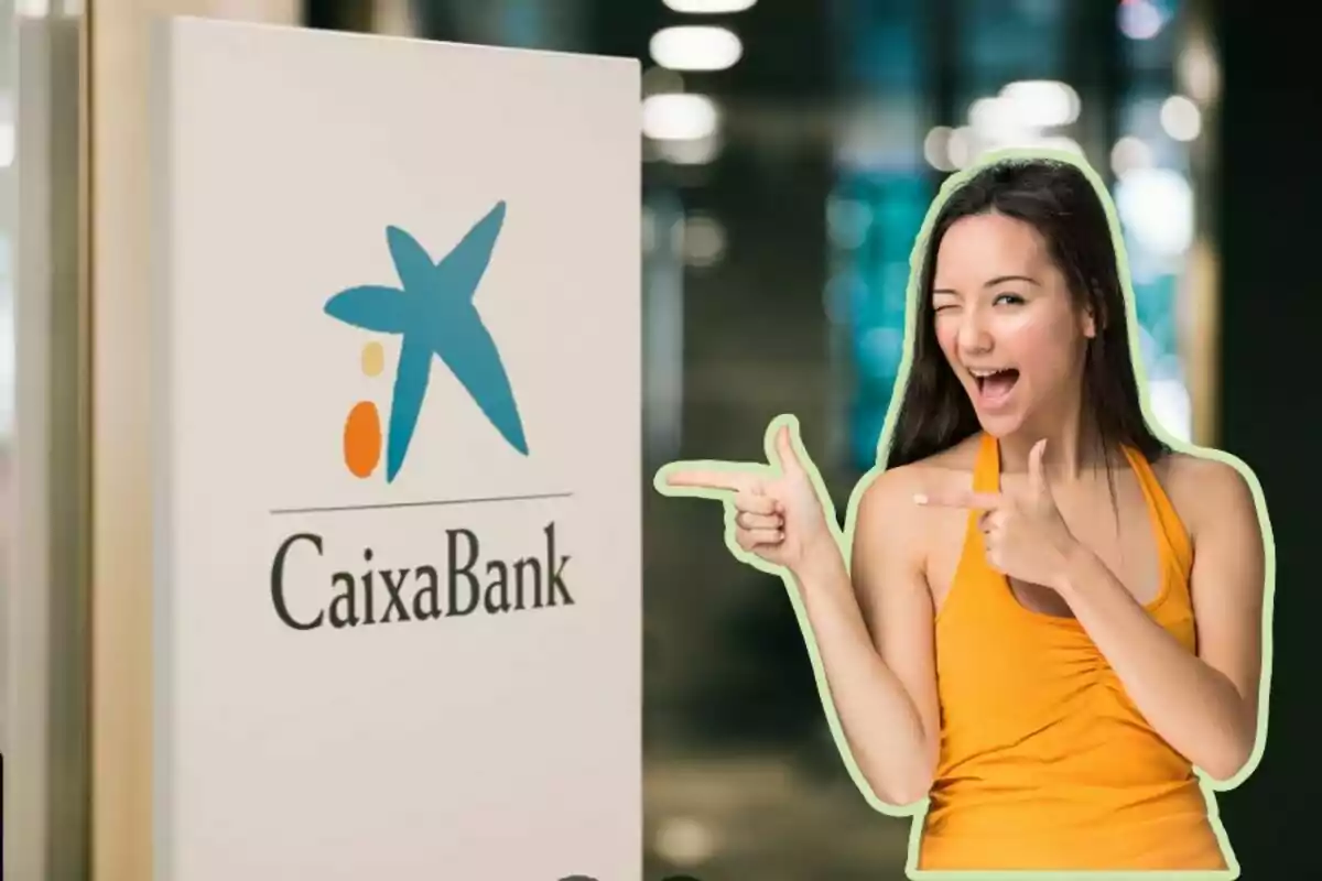 Una mujer sonriente con camiseta naranja señala con ambas manos hacia un cartel de CaixaBank.