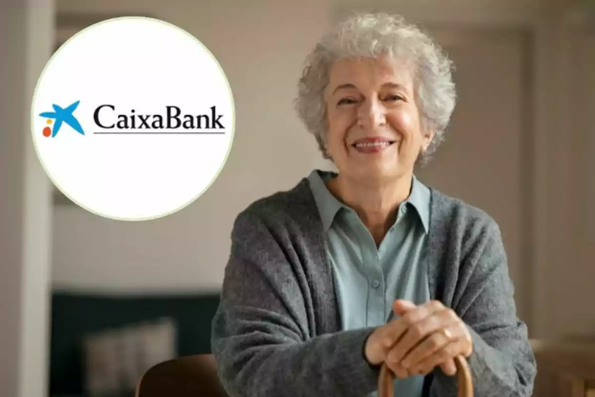 Una mujer mayor sonriente con cabello canoso y un suéter gris, apoyada en un bastón, con el logo de CaixaBank en la esquina superior izquierda.