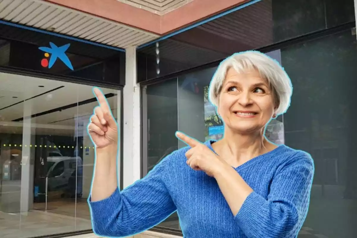 Mujer mayor sonriendo y señalando hacia el logotipo de una entidad bancaria en la entrada de un edificio.