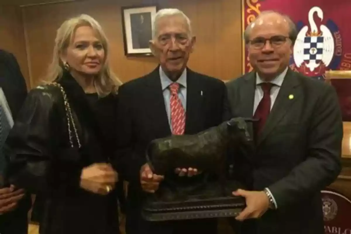 Tres personas posan para una foto mientras sostienen una estatua de un toro.