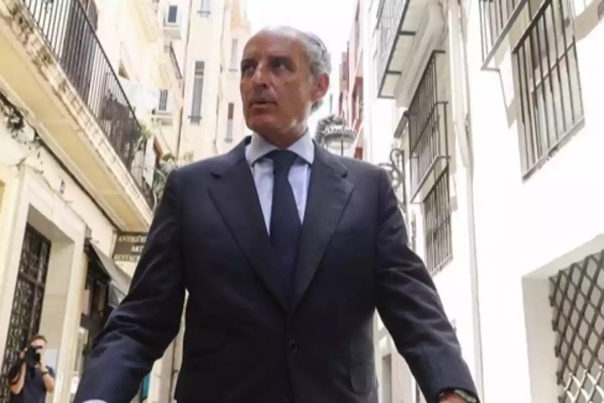 Un hombre con traje oscuro camina por una calle estrecha entre edificios.