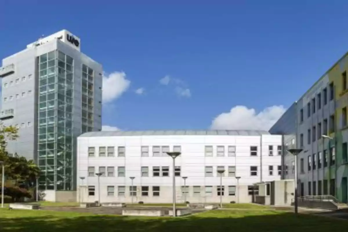 Edificio moderno de varios pisos con fachada de vidrio y metal rodeado de áreas verdes bajo un cielo azul despejado Edificio moderno de varios pisos con fachada de vidrio y metal rodeado de áreas verdes bajo un cielo azul despejado