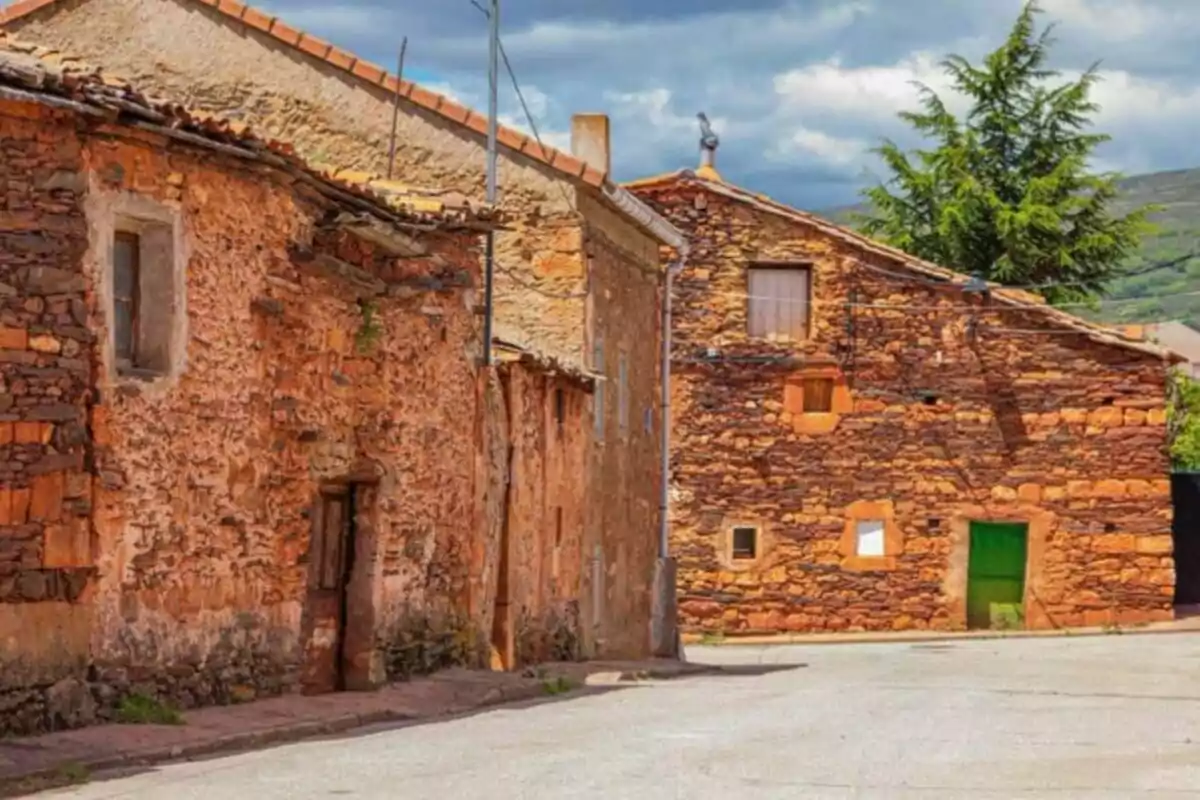 Una calle tranquila con casas de piedra de tonos rojizos y un cielo parcialmente nublado.