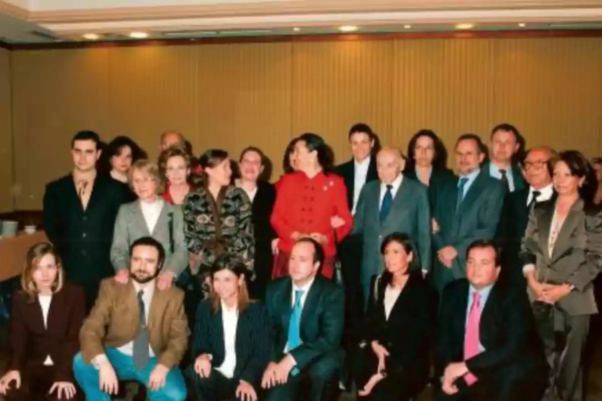 Un grupo de personas posando para una foto en un entorno formal, con algunos sentados y otros de pie, en una sala con paredes de madera y luces en el techo.