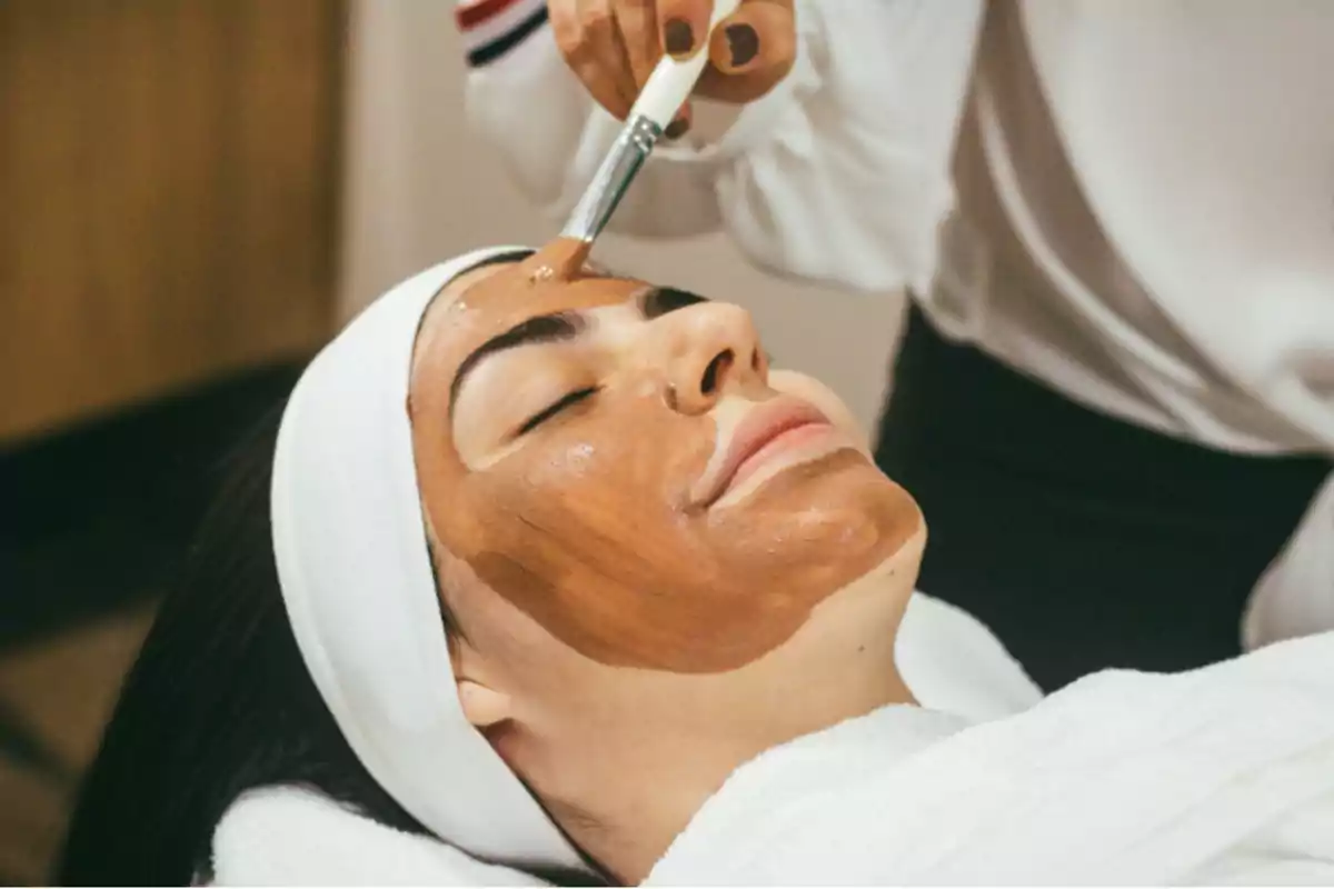 Persona recibiendo un tratamiento facial con una mascarilla de arcilla marrón.