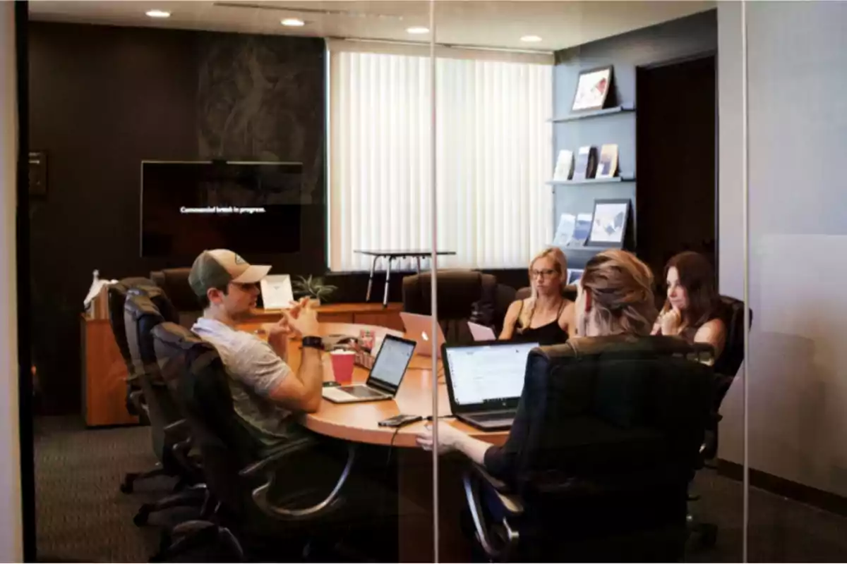 Reunión de trabajo en una sala de conferencias con cuatro personas usando laptops.