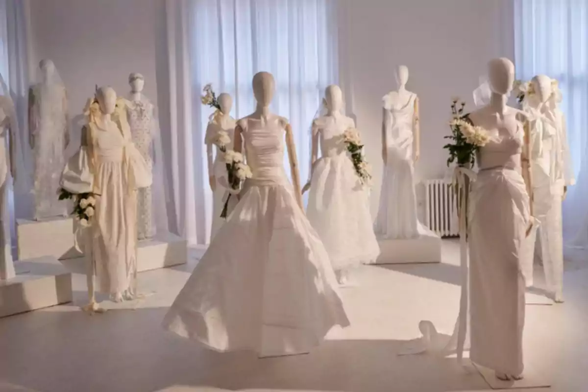Maniquíes vestidos con trajes de novia blancos, sosteniendo ramos de flores, en una habitación iluminada con cortinas blancas.