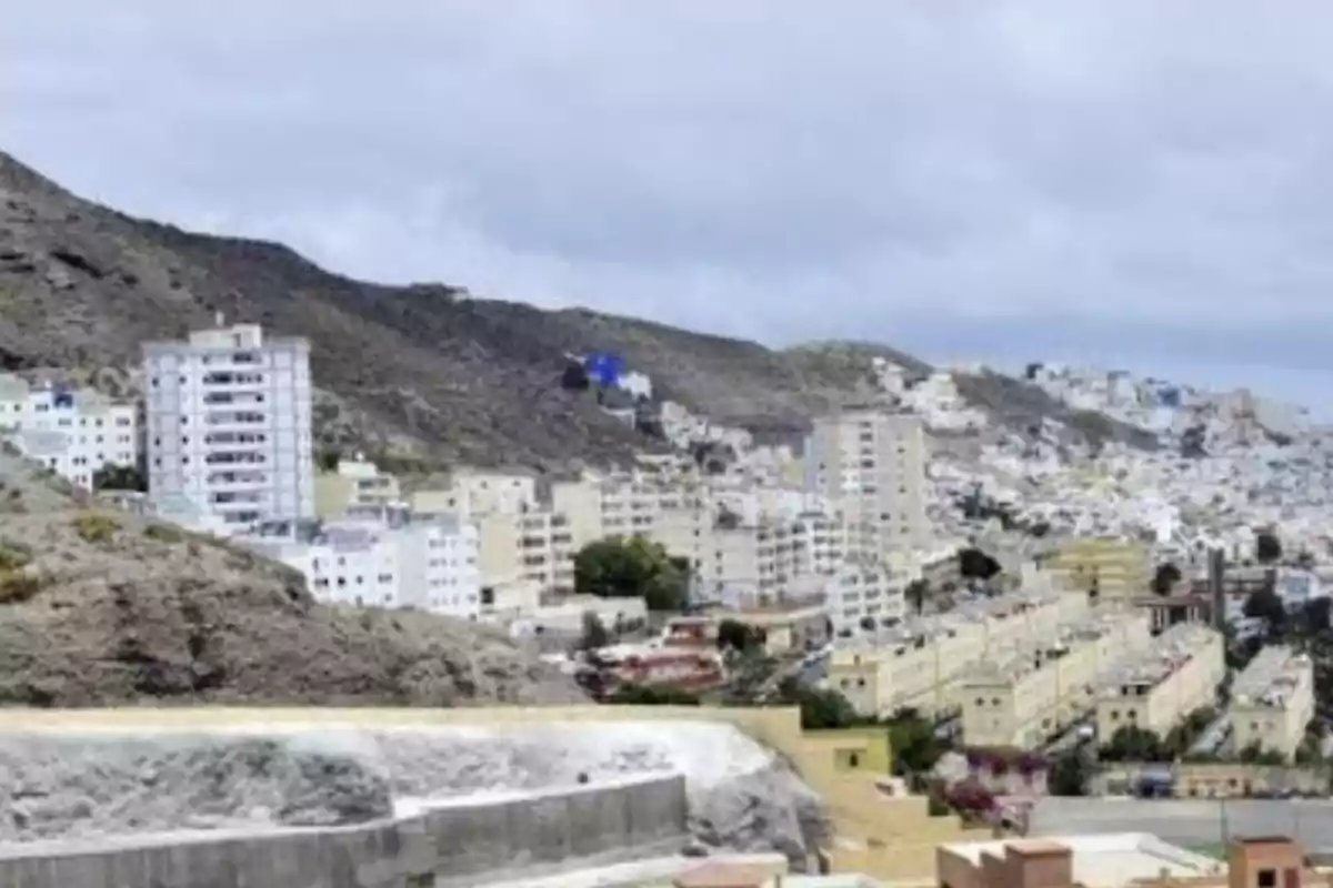 Vista de una ciudad con edificios altos y montañas en el fondo bajo un cielo nublado.