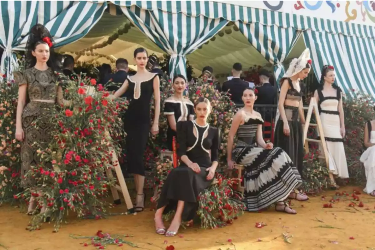 Un grupo de mujeres posando con vestidos elegantes en un entorno decorado con flores y una carpa a rayas verdes y blancas.