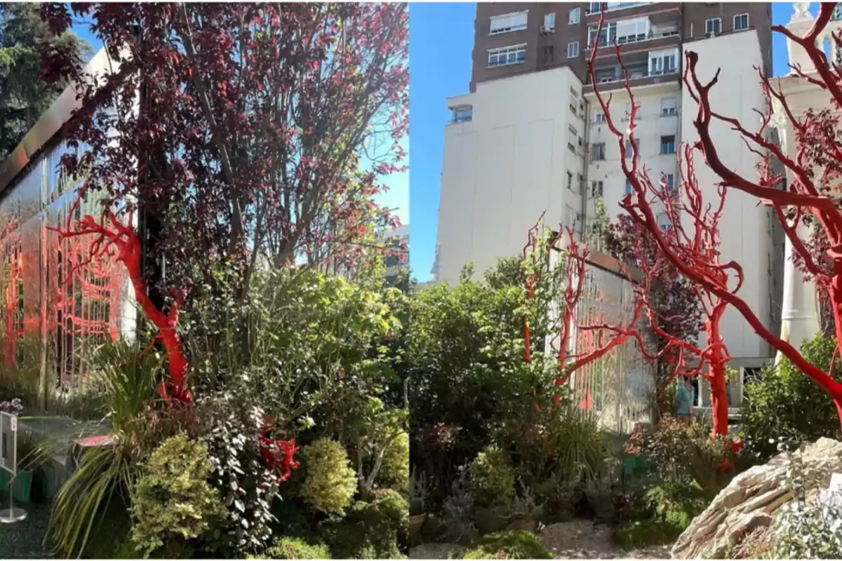Un jardín urbano con árboles y arbustos, algunos de los cuales tienen ramas pintadas de rojo, rodeado de edificios altos.