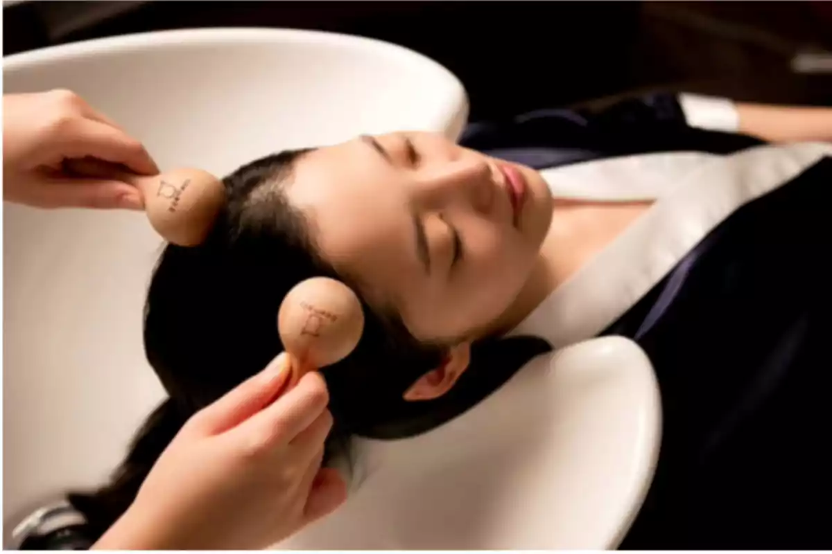 Persona recibiendo un masaje en la cabeza con herramientas de madera en un salón de belleza.