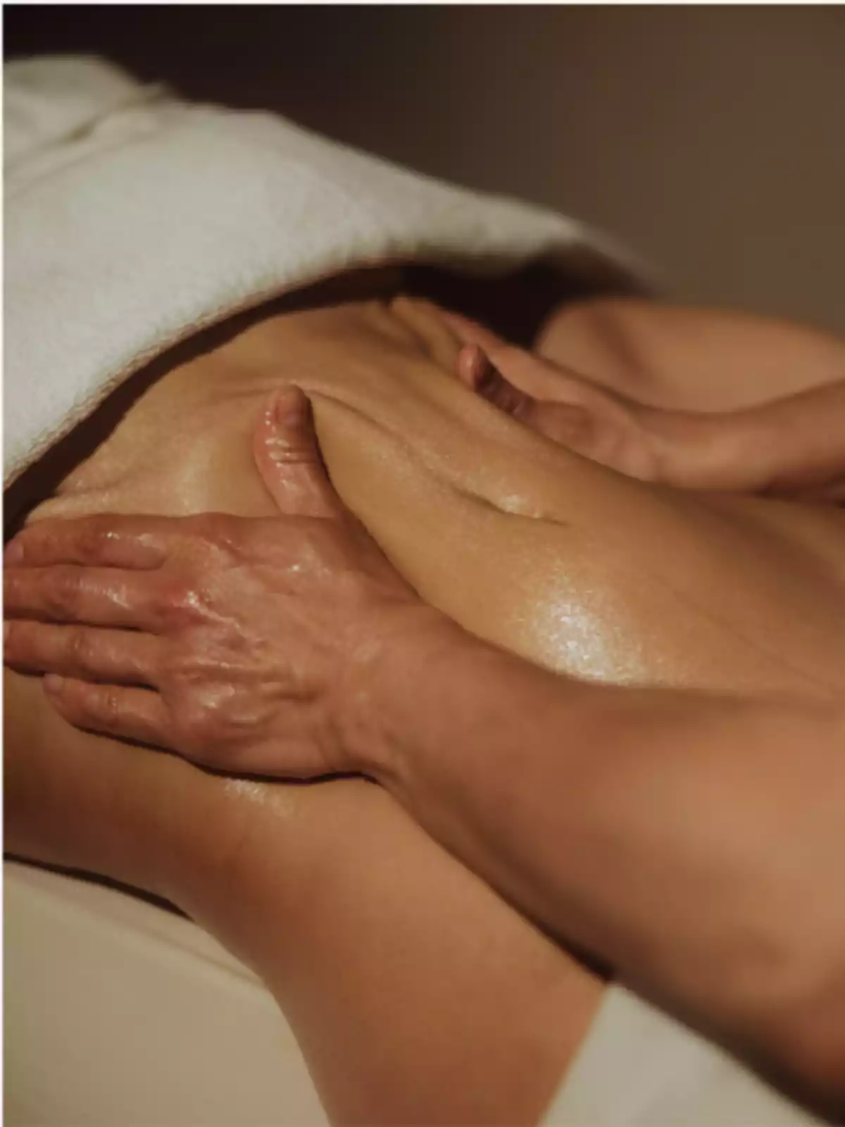 Persona recibiendo un masaje en la espalda con una toalla blanca cubriendo la parte superior del cuerpo.
