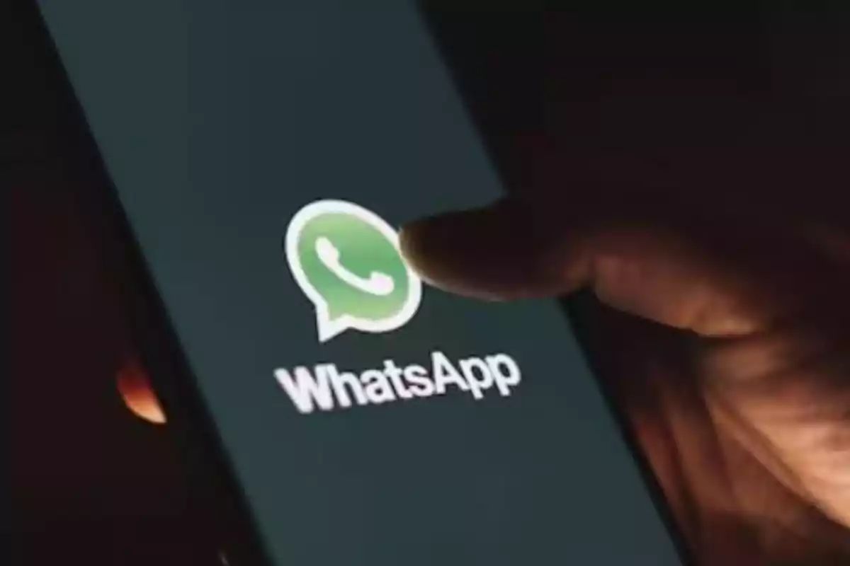 Pantalla de un teléfono móvil mostrando el logo de WhatsApp con un dedo a punto de tocarlo.