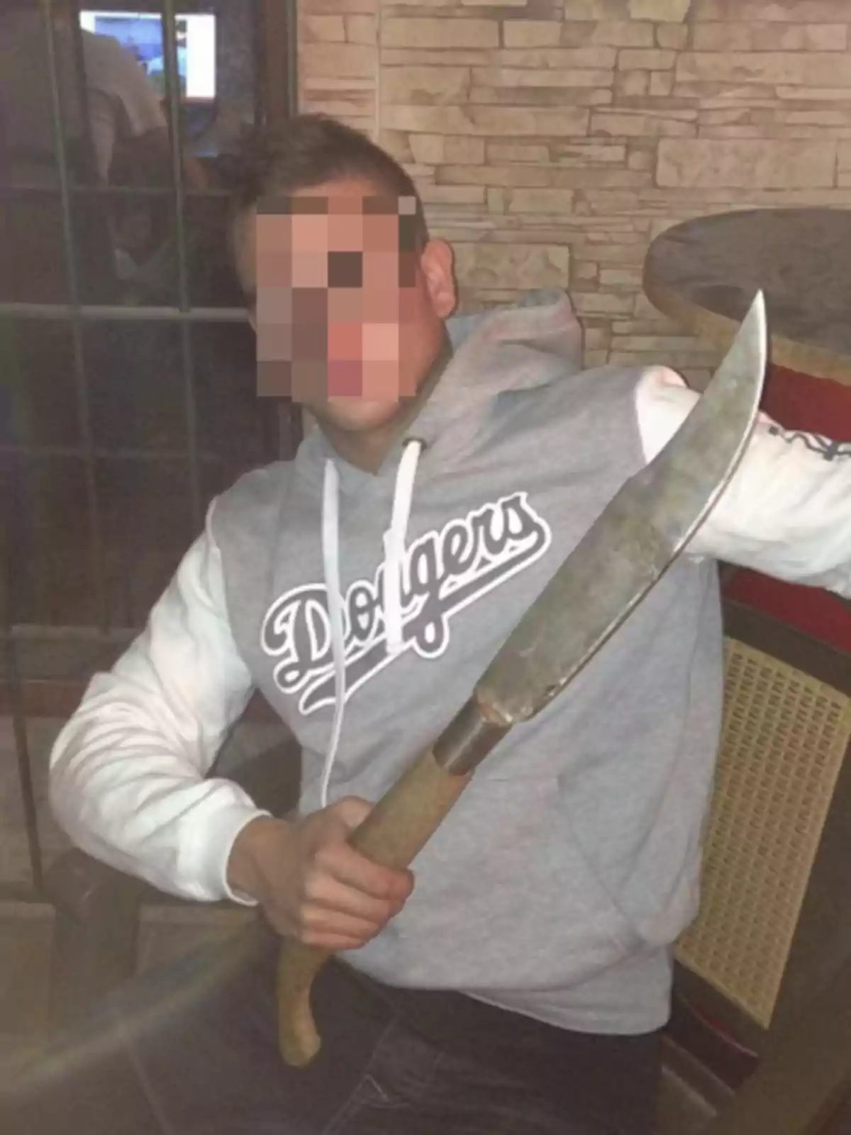 Una persona con el rostro pixelado sostiene un cuchillo grande mientras viste una sudadera con capucha que tiene la palabra 