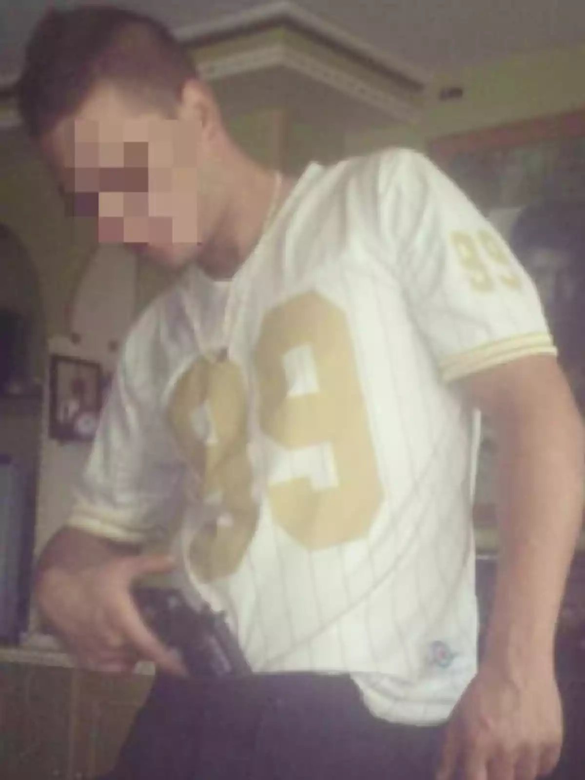 Un hombre con el rostro pixelado viste una camiseta blanca con el número 99 en dorado y sostiene una pistola.