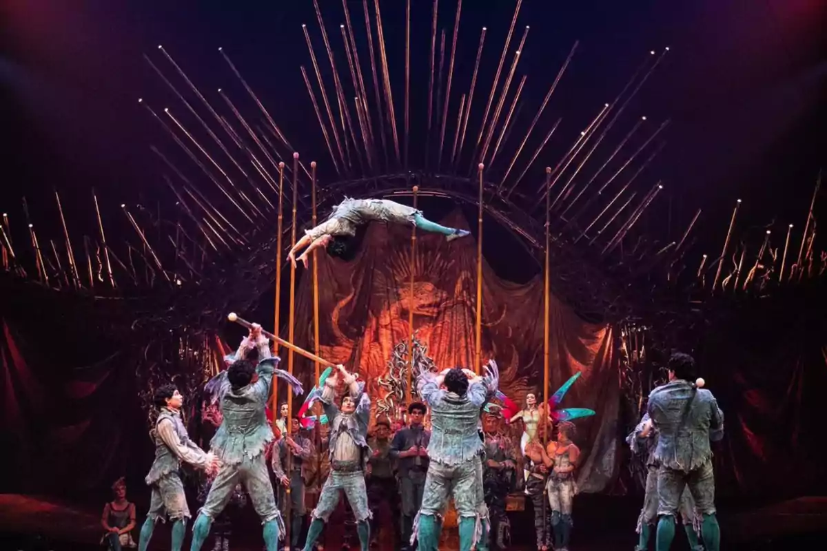 Artistas de circo realizando una acrobacia aérea en un escenario decorado con elementos teatrales y luces dramáticas.