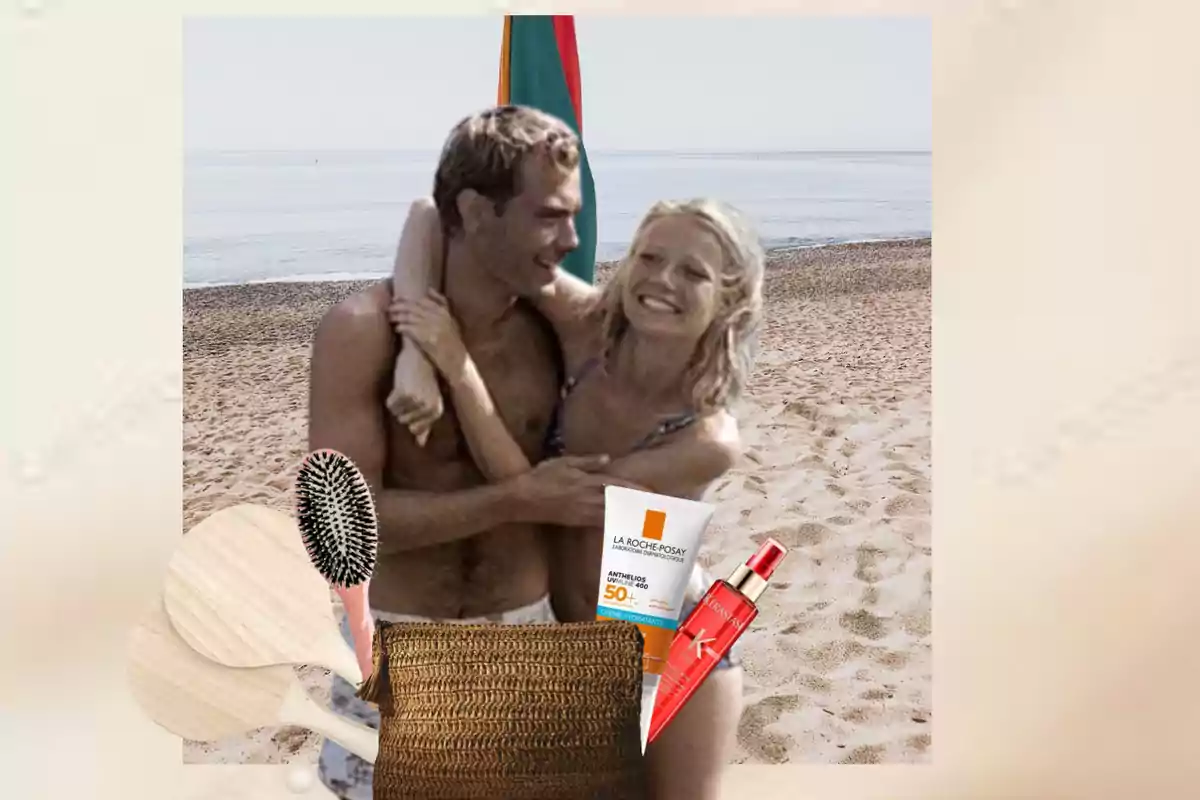 Una pareja abrazándose en la playa con artículos de playa en primer plano, incluyendo una crema solar, un cepillo, una bolsa de playa y un spray para el cabello.