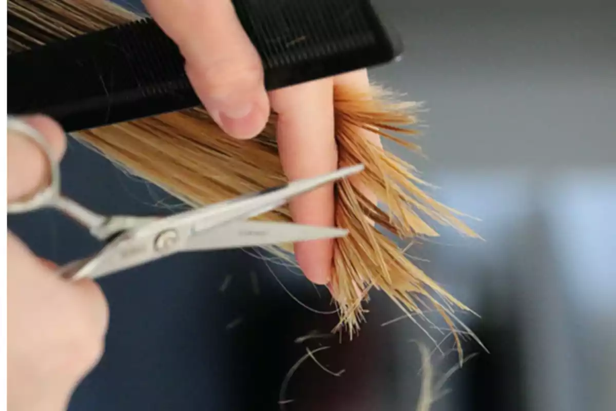 Manos cortando el cabello rubio con tijeras y un peine negro.