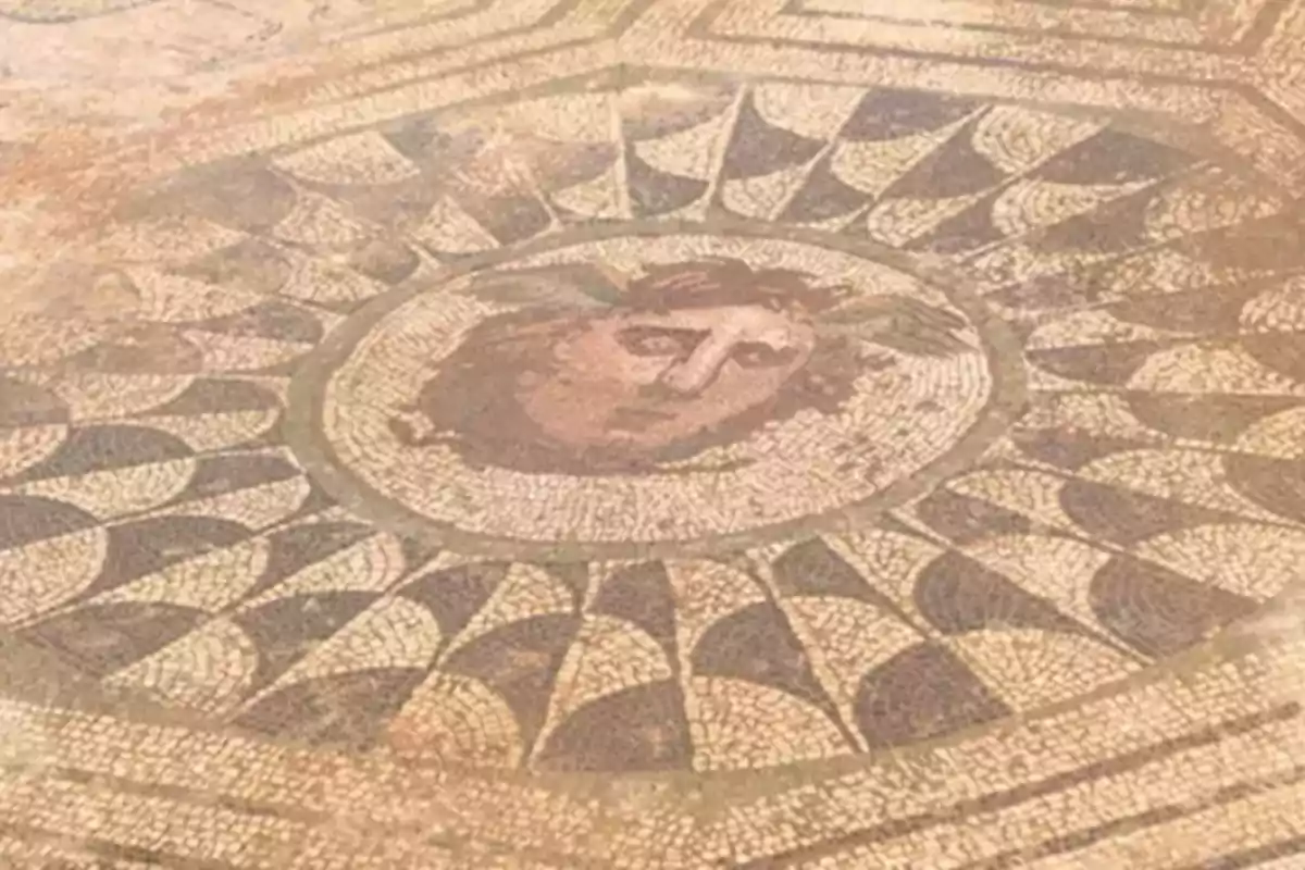 Mosaico antiguo con diseño geométrico y rostro en el centro.