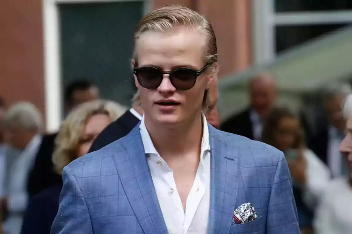 Hombre joven con gafas de sol y traje azul claro en un evento al aire libre.