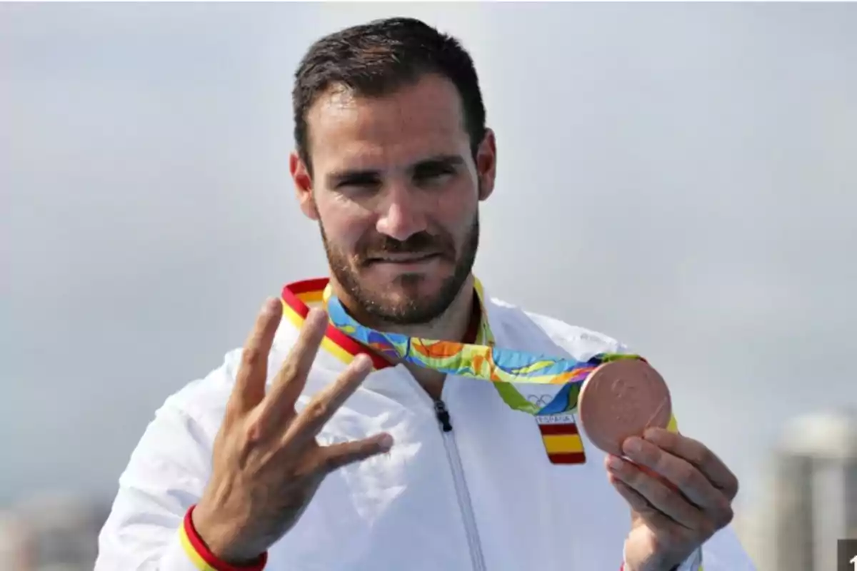 Un hombre con una medalla olímpica de bronce y mostrando cuatro dedos.