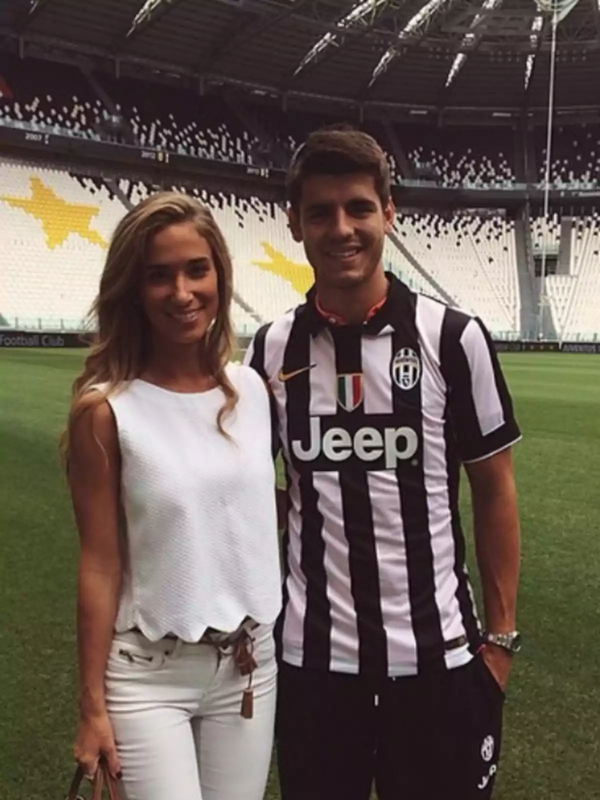 Una pareja posando en un estadio de fútbol, con el hombre vistiendo una camiseta de la Juventus y la mujer con una blusa blanca y pantalones claros.