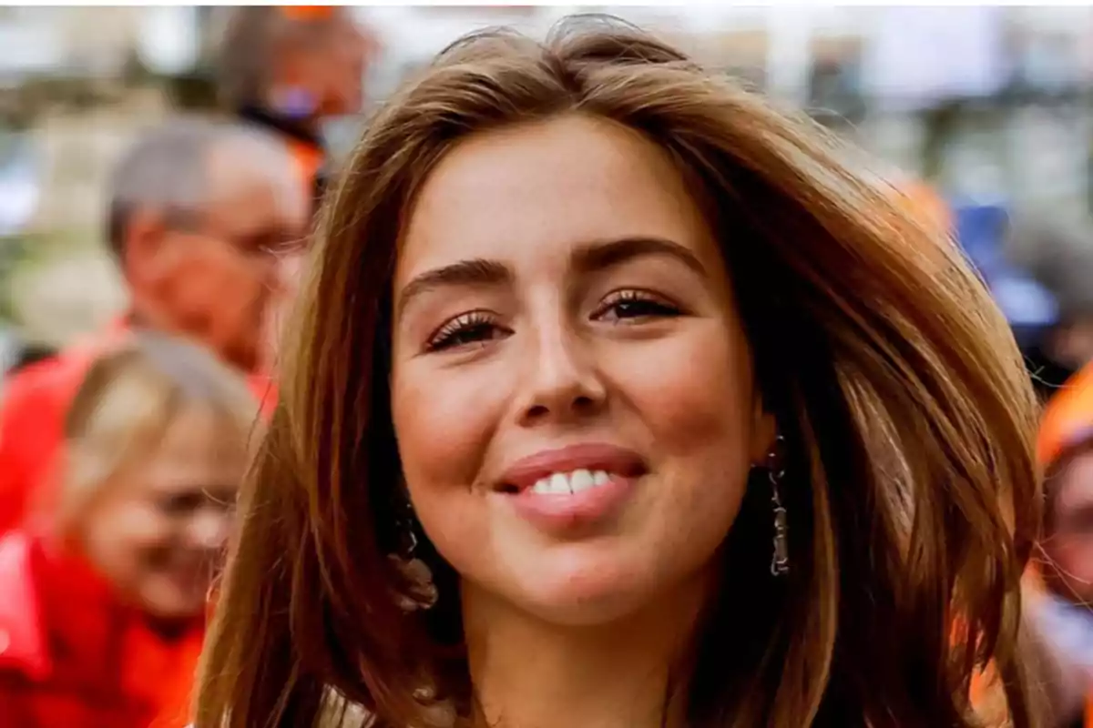 Una mujer joven sonriendo con el cabello suelto y un fondo desenfocado de personas.