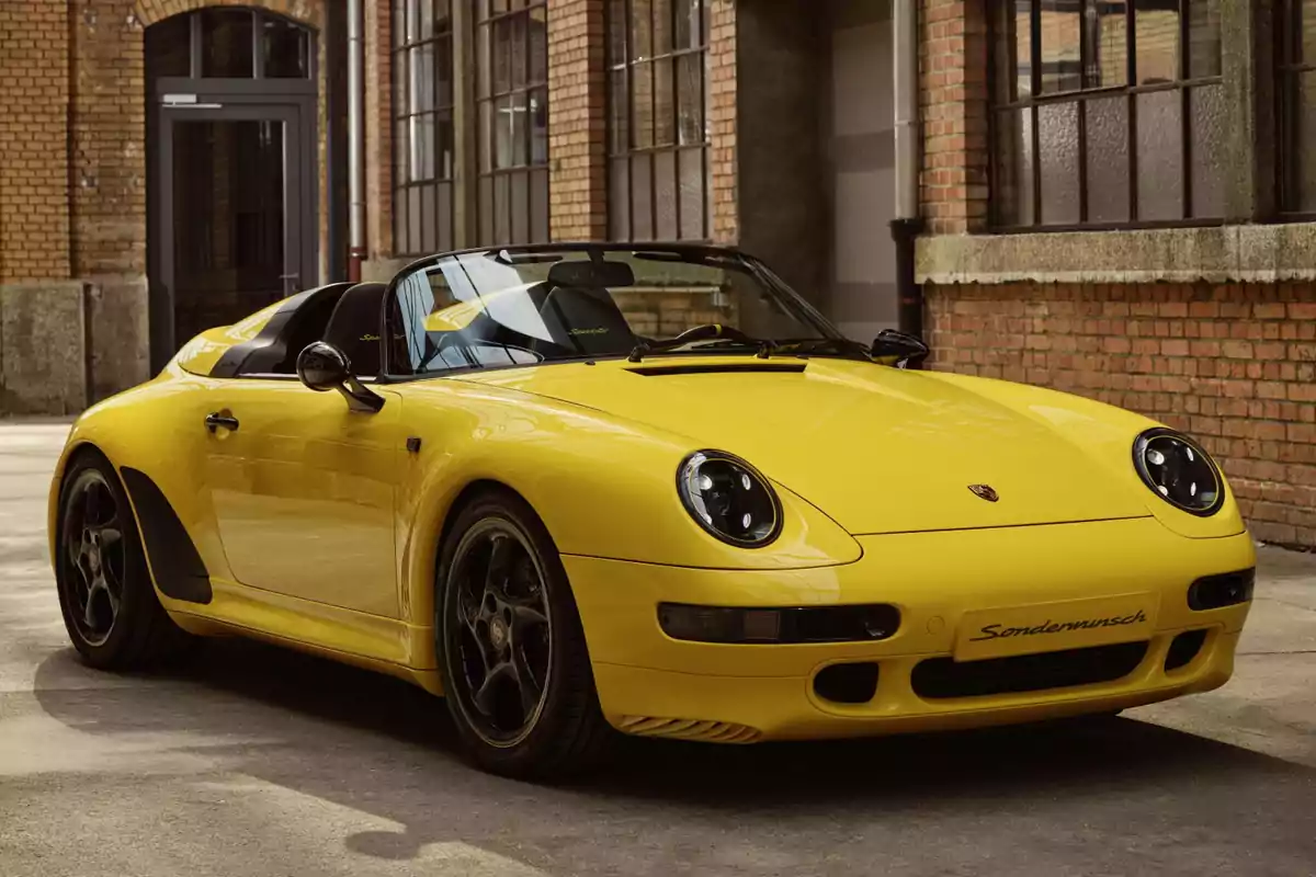 Un coche Porsche 911 Speedster único deportivo amarillo estacionado frente a un edificio de ladrillos.