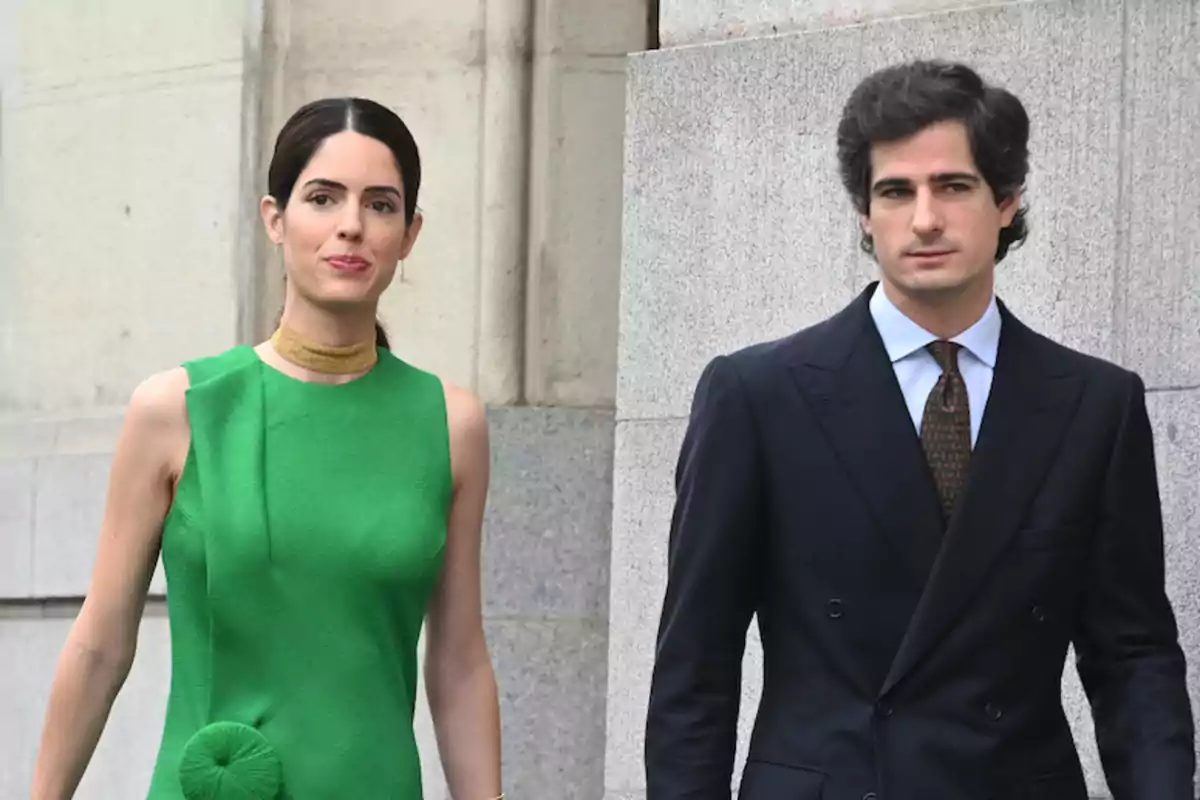 Una mujer con vestido verde y un hombre con traje oscuro caminando juntos.