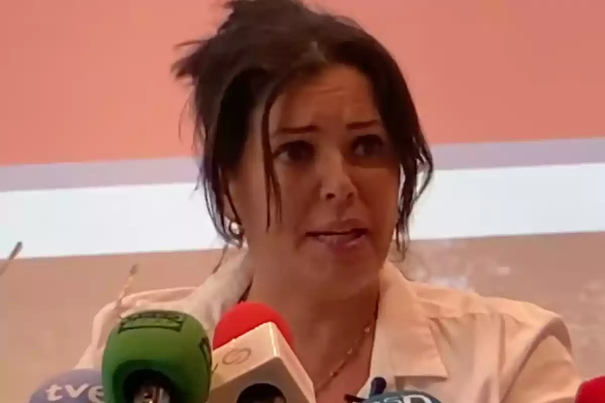 Mujer hablando en una conferencia de prensa con varios micrófonos frente a ella.