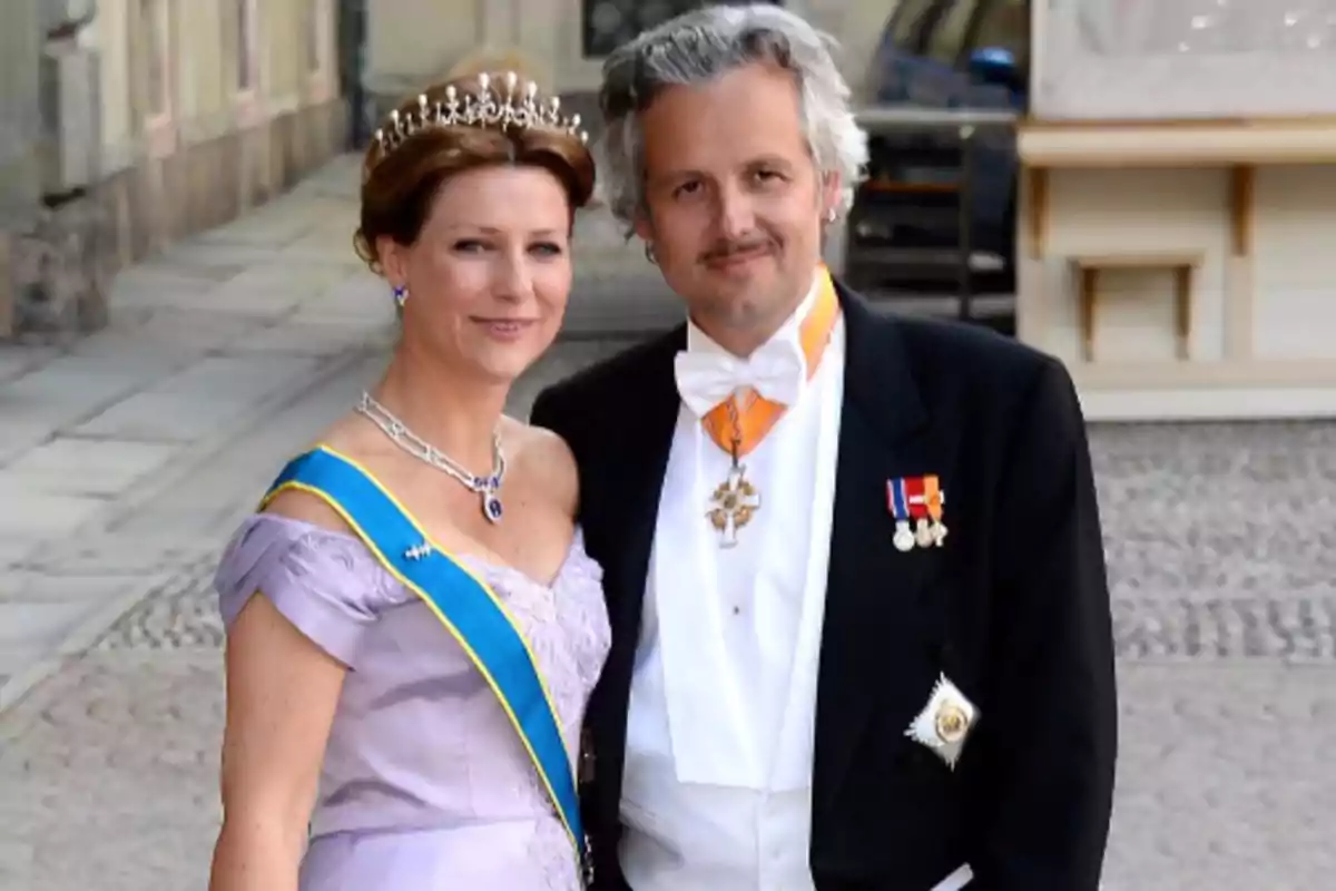 Una pareja vestida de gala, con la mujer usando una tiara y una banda azul, y el hombre con un traje formal y medallas.