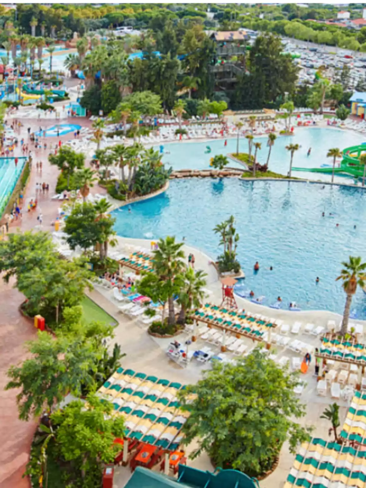 Vista aérea de un parque acuático con piscinas, toboganes y áreas de descanso rodeadas de vegetación y palmeras.