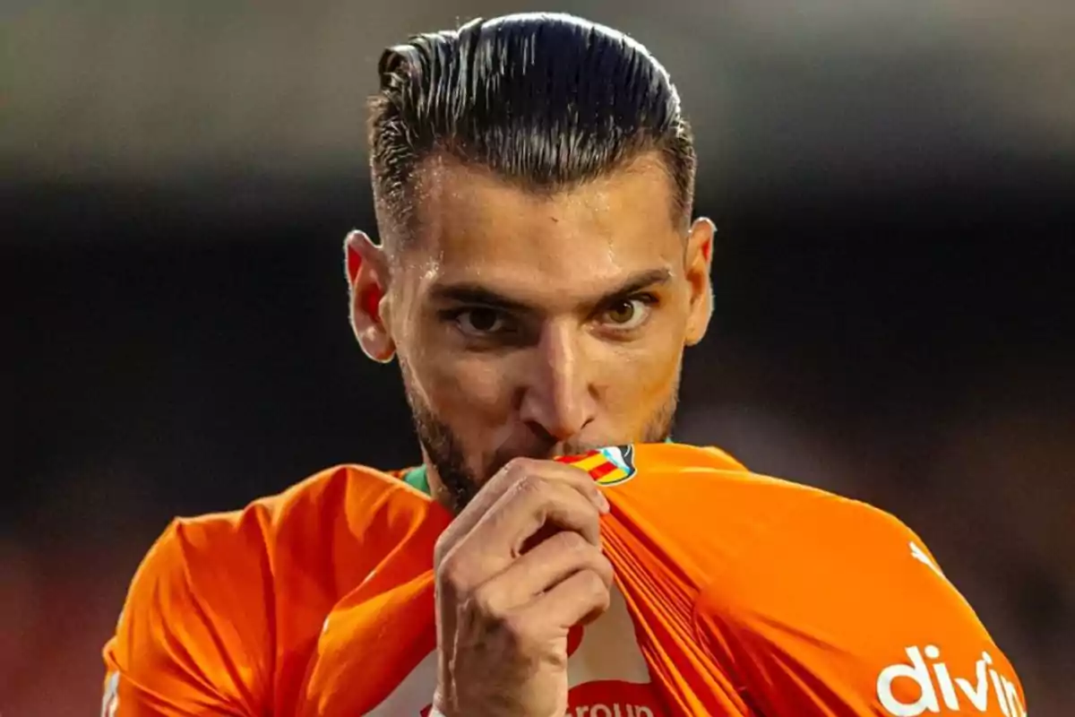 Un jugador de fútbol besa el escudo de su camiseta naranja durante un partido.