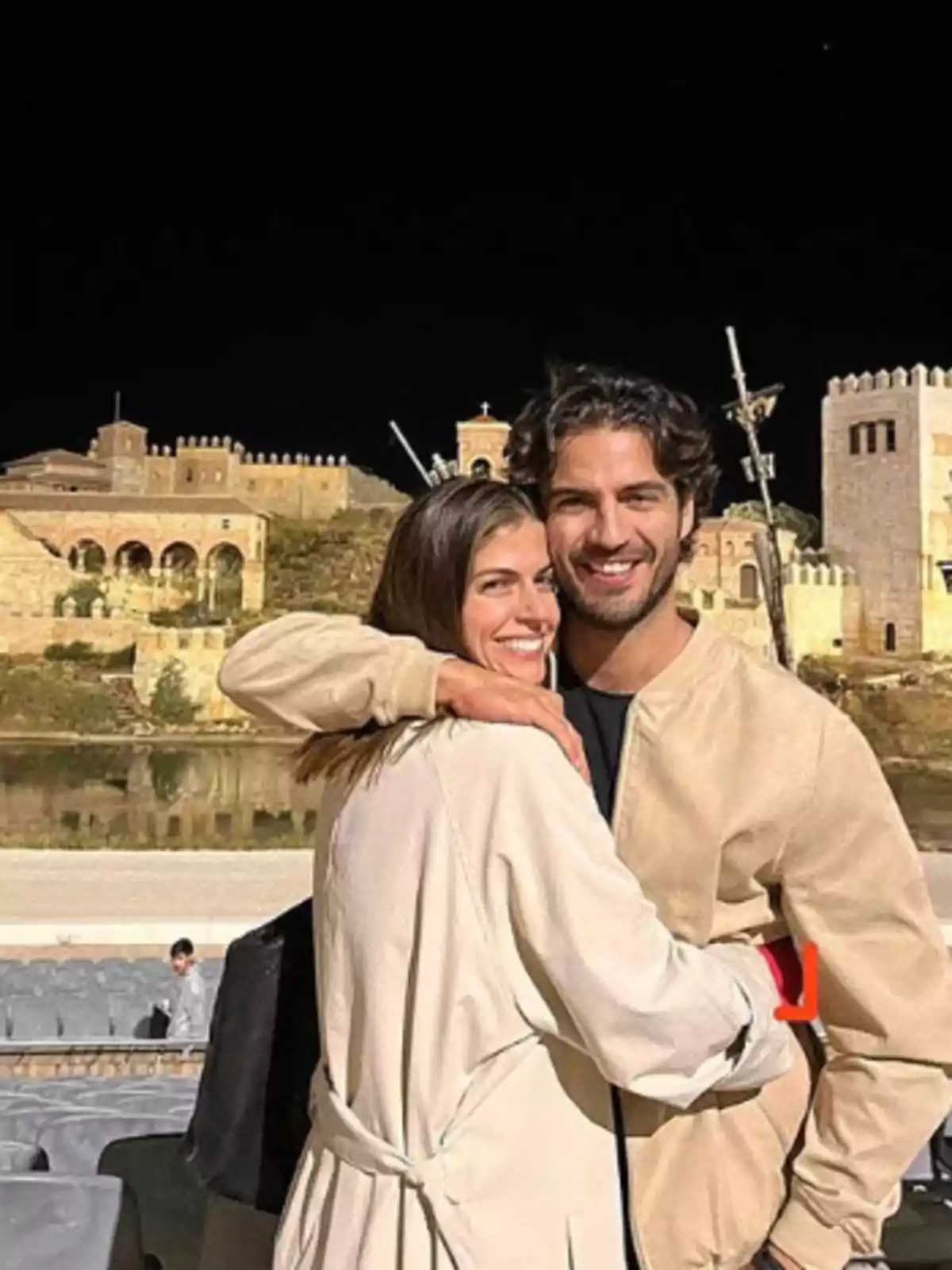 Una pareja abrazándose frente a un edificio histórico iluminado por la noche.