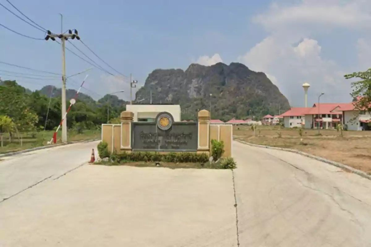 Entrada a un complejo con un letrero en un idioma asiático, rodeado de montañas y edificios con techos rojos.