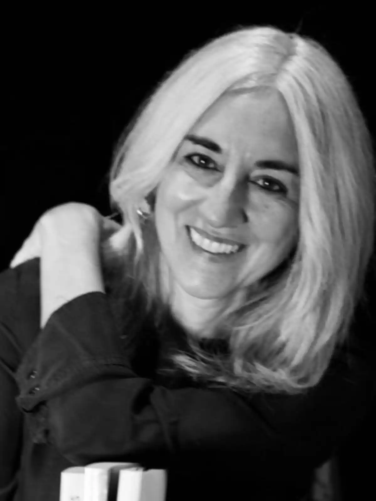 Mujer de cabello canoso y largo sonriendo en una fotografía en blanco y negro.