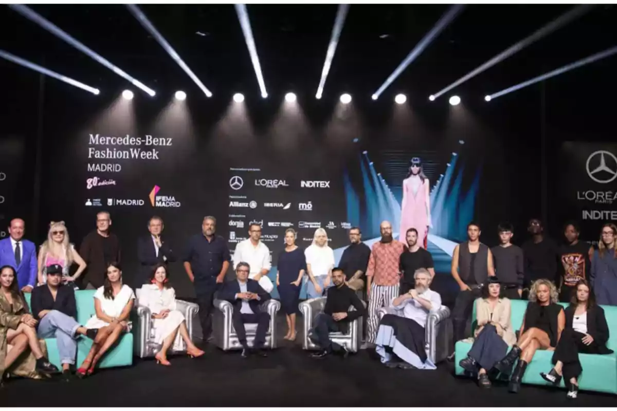 Grupo de personas posando en el escenario de la Mercedes-Benz Fashion Week Madrid, con logotipos de patrocinadores en el fondo.